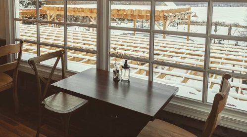 A cozy dining area with a table set for two, featuring a view of mountains and a sign announcing indoor dining tomorrow.
