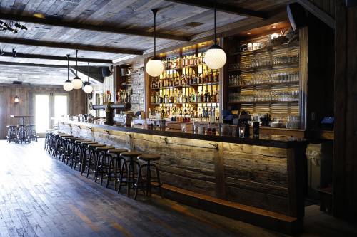 A rustic bar with wooden decor, shelves lined with bottles, and stools arranged along the counter. Warm lighting enhances the ambiance.