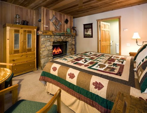 Cozy cabin bedroom with a stone fireplace, wooden furniture, and a quilted bedspread featuring nature motifs.
