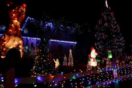 A festive display of colorful Christmas lights, featuring a reindeer, snowman, and decorated trees in a yard.