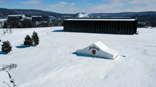A snowy landscape featuring a large white building with "Jim Beam" signage and a dark warehouse in the background.