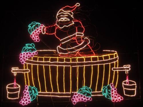 A festive light display featuring Santa Claus in a barrel, surrounded by grapevines and buckets.
