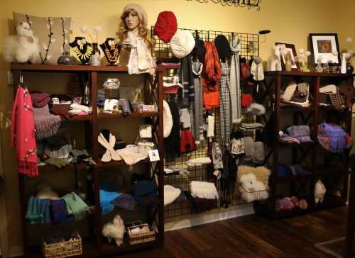 A cozy display of various scarves, hats, and accessories on wooden shelves against a warm yellow wall.