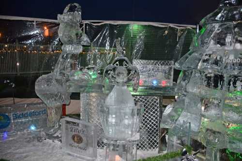 A display of intricate ice sculptures, including a penguin and a tree, illuminated with colorful lights.