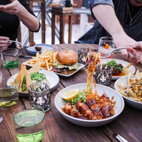 A table filled with various dishes, including fries, a burger, salad, and grilled chicken, with drinks in green glasses.