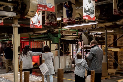 Visitors explore a sports memorabilia factory, surrounded by banners of famous players and equipment in the background.