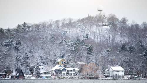 Snow-covered houses along a lake, with a snowy hillside and a radar dome in the background.