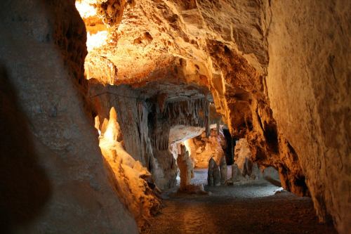 A dimly lit cave with stalactites and stalagmites, showcasing natural rock formations and illuminated areas.