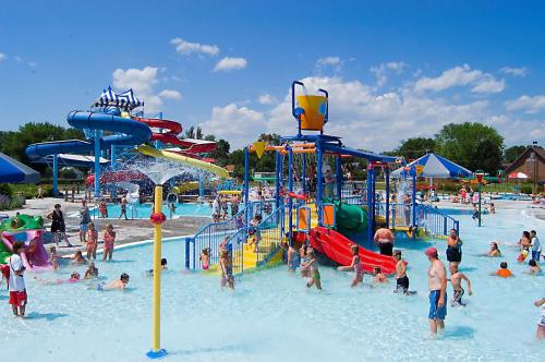 A vibrant water park scene with children playing in pools, water slides, and colorful play structures under a sunny sky.