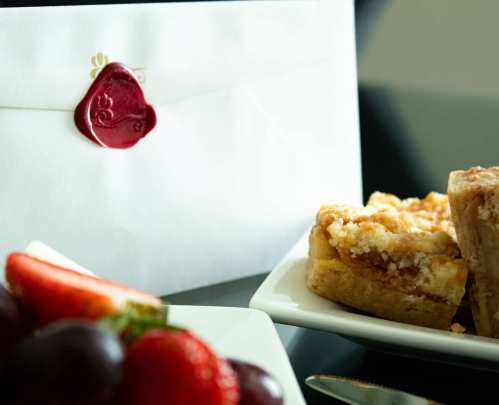 An envelope with a wax seal beside a plate of dessert bars and fresh strawberries on a table.