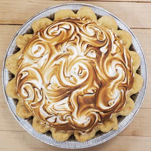 A beautifully baked pie with a golden-brown meringue topping, swirled and set in a silver pie dish.