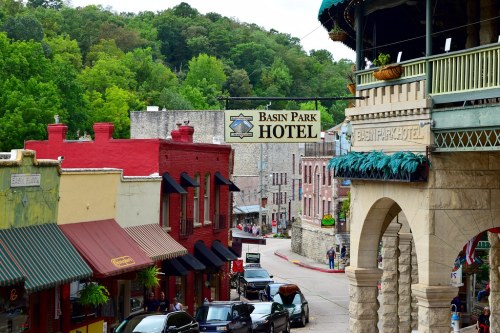 View of Basin Park Hotel sign with colorful buildings and trees in the background, showcasing a charming street scene.