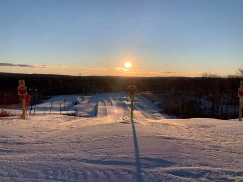 Sunset over a snowy ski slope, with numbered markers in the foreground and a clear sky in the background.