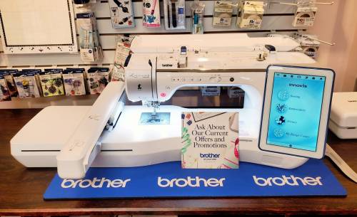 A Brother sewing machine displayed on a table with promotional materials and accessories in the background.