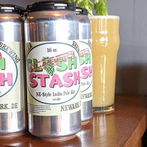 Three cans of "Stash" NE-Style India Pale Ale next to a glass of pale beer on a wooden table.