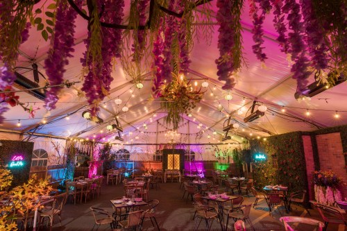 A vibrant indoor event space with colorful lighting, floral decorations, and tables set for dining.