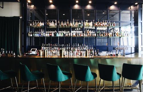 A stylish bar with a variety of liquor bottles displayed on shelves and green chairs in front.