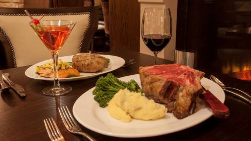 A gourmet dinner featuring a large steak, mashed potatoes, broccoli, a baked potato, a glass of red wine, and a cocktail.