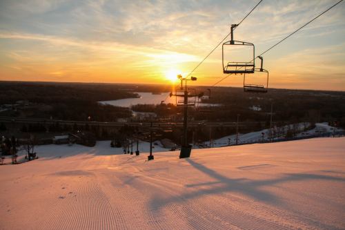 A sunset over a snowy ski slope, with ski lifts and a lake visible in the distance.