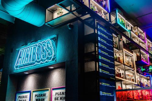 A vibrant bar interior featuring neon signage and shelves lined with various bottles. Colorful lighting enhances the atmosphere.