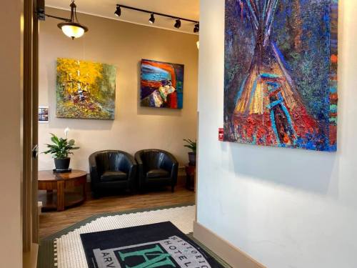 A hallway with colorful artwork on the walls, two black chairs, and a decorative rug at the entrance of a hotel.