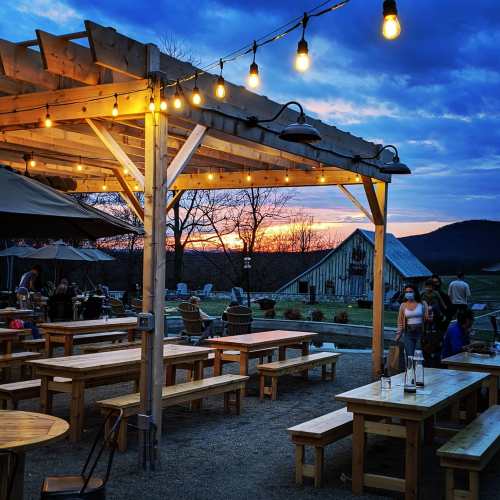 A rustic outdoor dining area with wooden tables, string lights, and a sunset in the background.