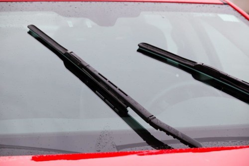 Close-up of a car windshield with wipers positioned in the upright position, raindrops visible on the glass.