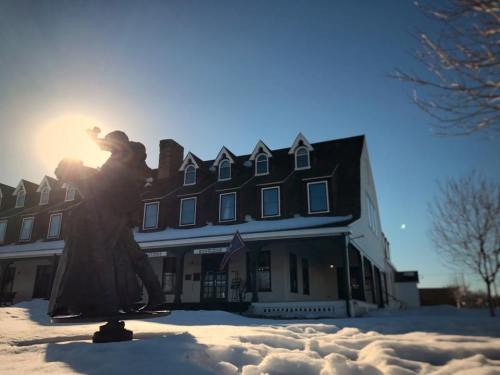 A statue in the foreground with sunlight behind it, snow covering the ground, and a historic building in the background.