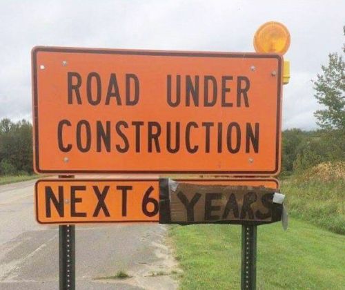 Orange road construction sign indicating work will continue for the next six years, with a taped-over section.