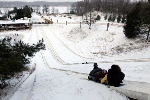 A snowy hill with people sledding down, surrounded by trees and a winter landscape.