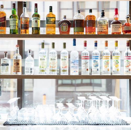 A well-stocked bar shelf featuring various bottles of liquor and glassware, with a bright window in the background.