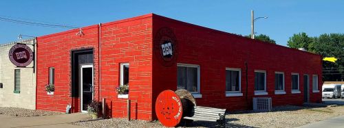 A bright red BBQ restaurant with a logo, windows, and a bench outside, set against a clear blue sky.