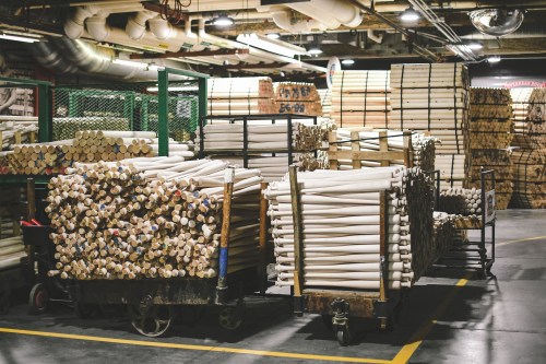A warehouse filled with stacked wooden materials and carts loaded with rolled items, organized in a spacious area.