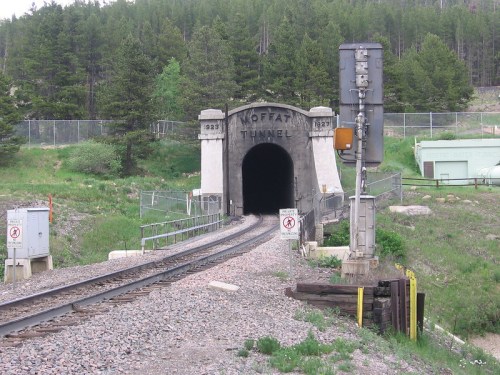 Entrance to the Moffat Tunnel, surrounded by greenery and railway tracks, with a signal post nearby.
