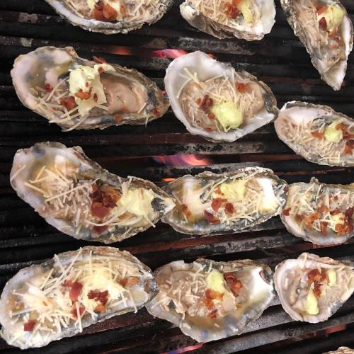 Grilled oysters topped with cheese, bacon, and herbs on a platter.