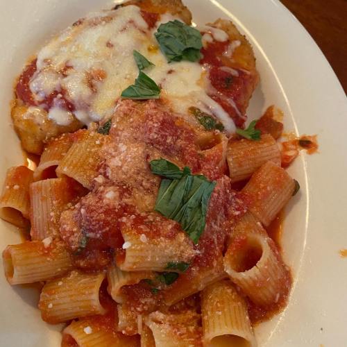 A plate of pasta with marinara sauce, topped with basil and cheese, alongside a breaded chicken cutlet with sauce.