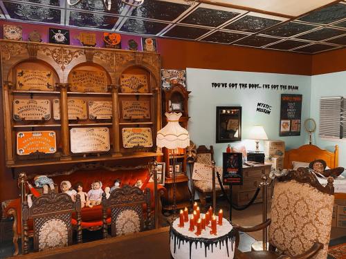 A vintage room with eerie decor, including a Ouija board, dolls, and a cake with candles, creating a spooky atmosphere.