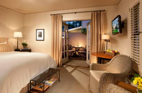 Cozy bedroom with a bed, armchair, and open doors leading to a patio with outdoor seating. Warm lighting and decor.