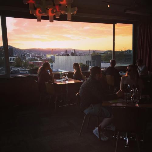 A sunset view from a restaurant with diners enjoying their meals, overlooking a cityscape.