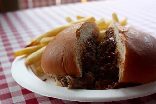 A close-up of a split sandwich filled with meat, served with a side of golden French fries on a checkered tablecloth.