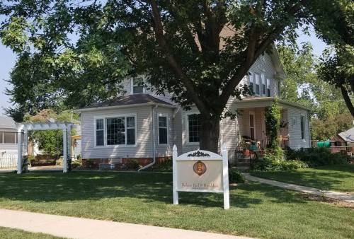 A charming two-story house with a large tree in the front yard and a sign that reads "Bed and Breakfast."