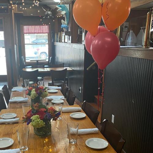 A dining table set with plates and glasses, decorated with flowers and balloons in a cozy restaurant setting.