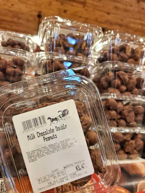 A clear plastic container filled with milk chocolate double peanuts, priced at $3.47, with stacked containers in the background.