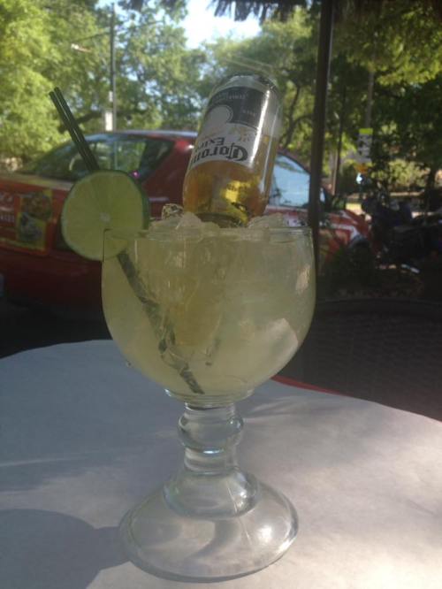 A large cocktail glass filled with ice and a lime slice, topped with a bottle of Corona beer.