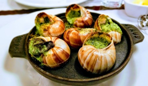 A dish of escargot in shells, baked with garlic herb butter, served in a round cast iron dish.