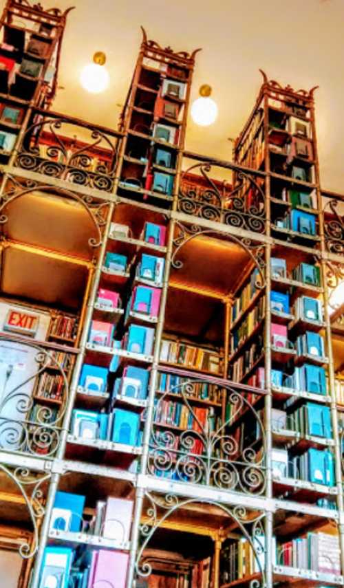 A beautifully designed library with ornate shelves filled with colorful books and an exit sign visible.