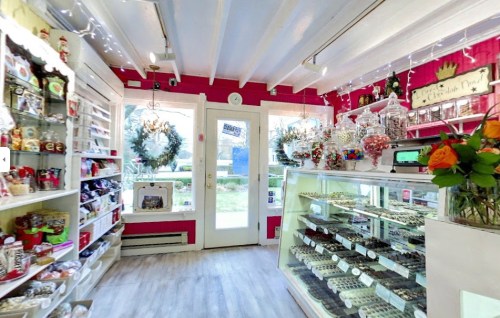 A cozy candy shop with colorful shelves, glass jars of sweets, and festive decorations, featuring a welcoming entrance.