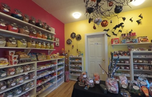 A colorful candy shop filled with jars of sweets, decorated with Halloween-themed ornaments and bats.