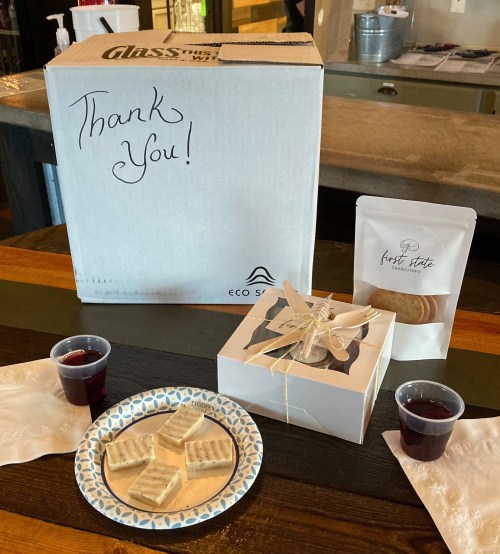A thank you box with treats, a small cake, and two cups of red drink on a table.