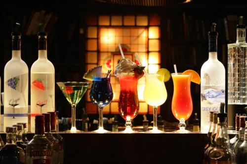 A variety of colorful cocktails displayed on a bar, with bottles of liquor in the foreground and a warm background glow.